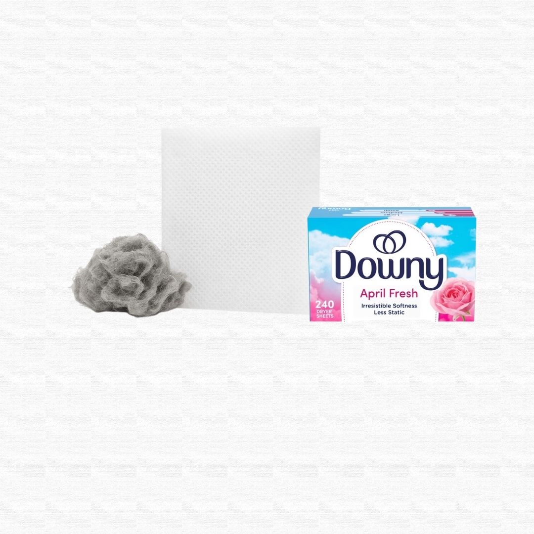 A handful of gray laundry dryer lint next to a used dryer sheet